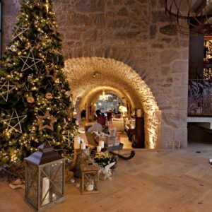 Decoración navideña en el hotel La Vella Farga, en el Solsonès, con un gran árbol iluminado, velas y faroles en un salón de piedra.