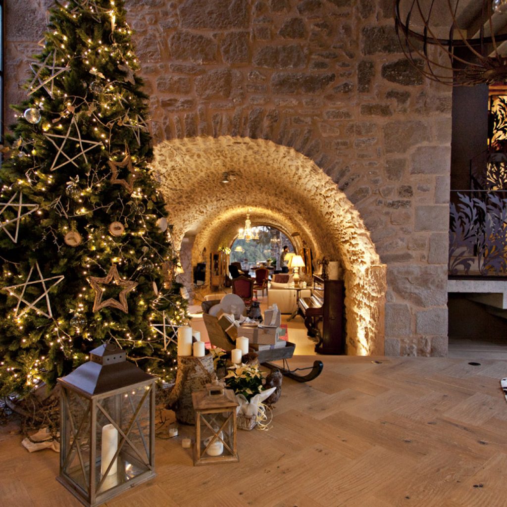 Decoración navideña en el hotel La Vella Farga, en el Solsonès, con un gran árbol iluminado, velas y faroles en un salón de piedra.